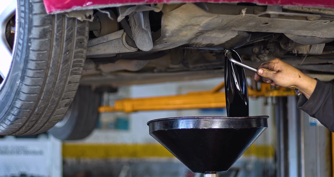 A mechanic's hand underneath a vehicle performing an oil change 